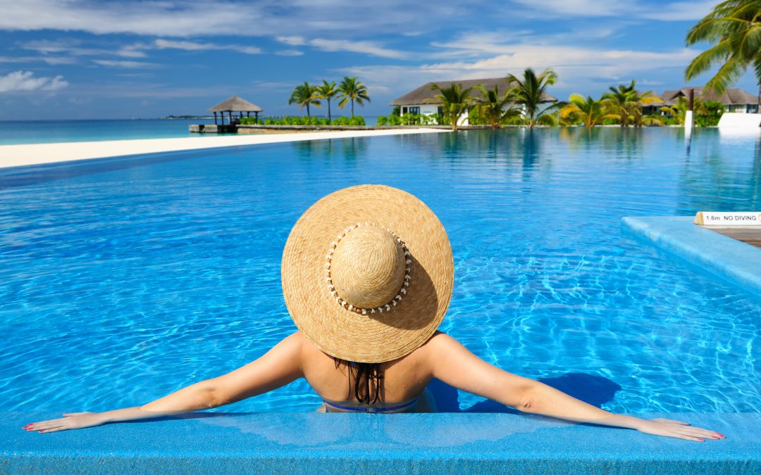 Frau mit Sonnenhut entspannt am Pool und genießt die Sonne